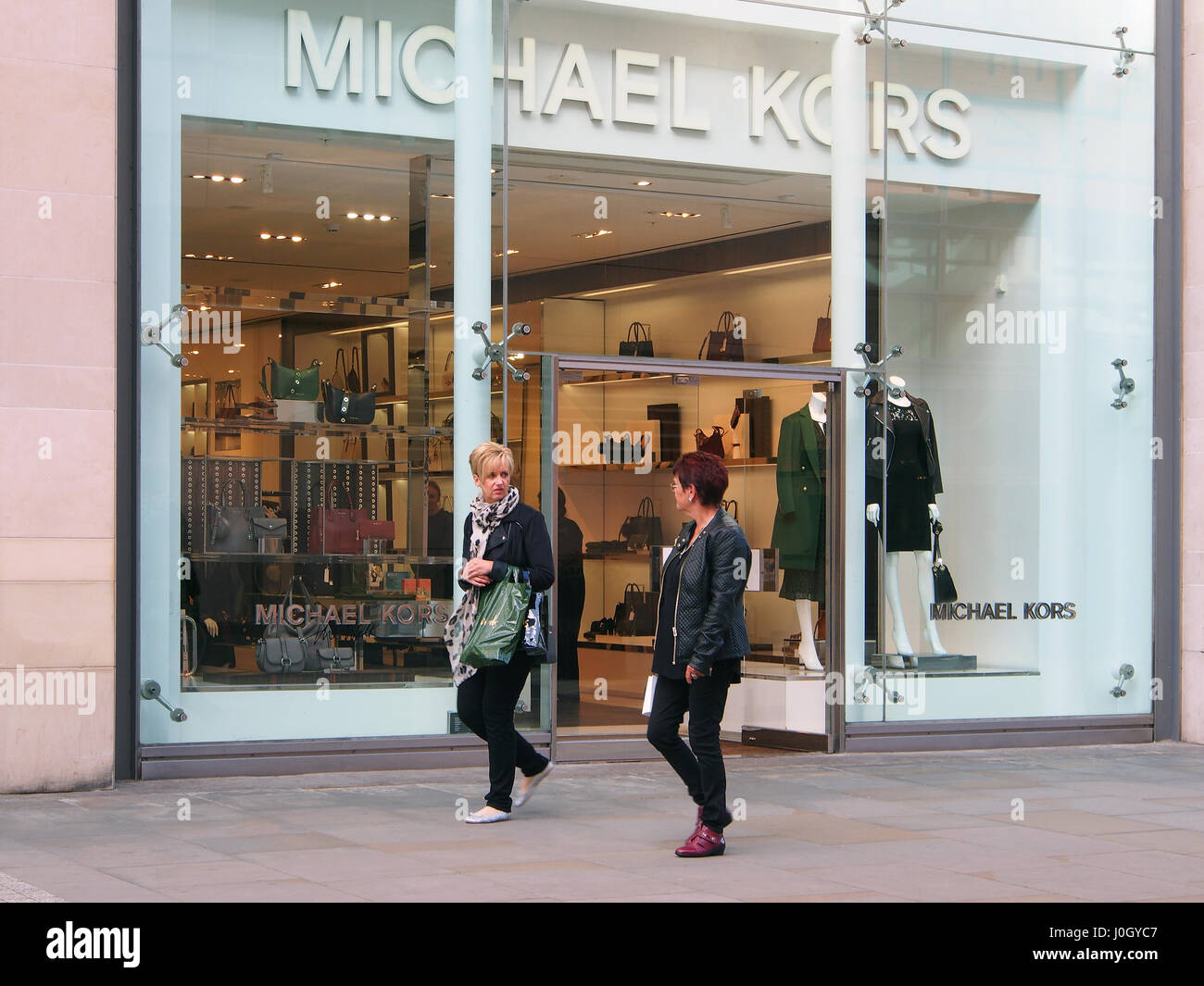 Fashionable Manchester shop shops Michael Kors in the city centre center showing the window display and two caucasian women in the foreground. Stock Photo