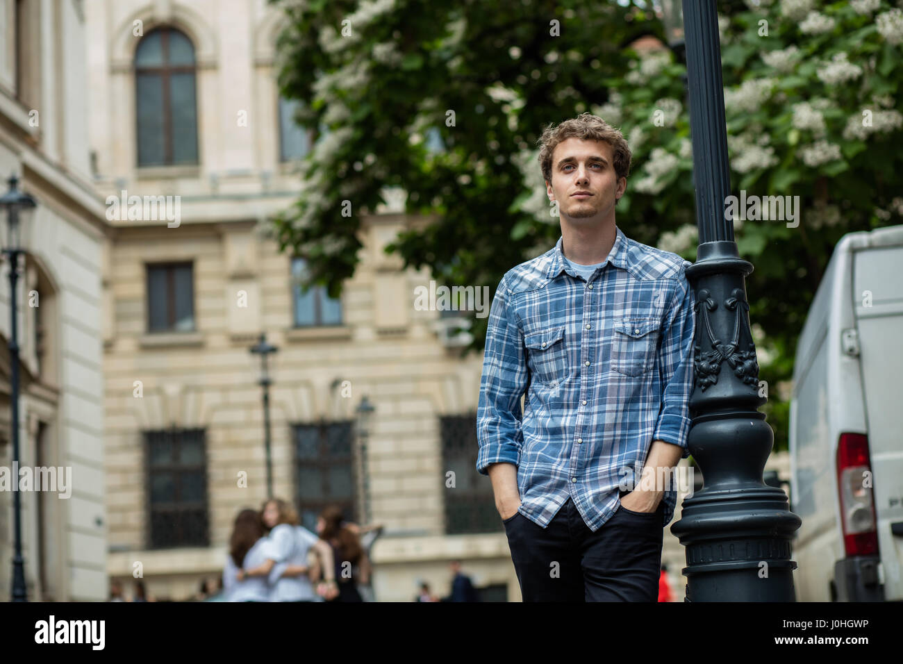 young blond and curly man with checkered shirt standing outside near a lamppost street Stock Photo