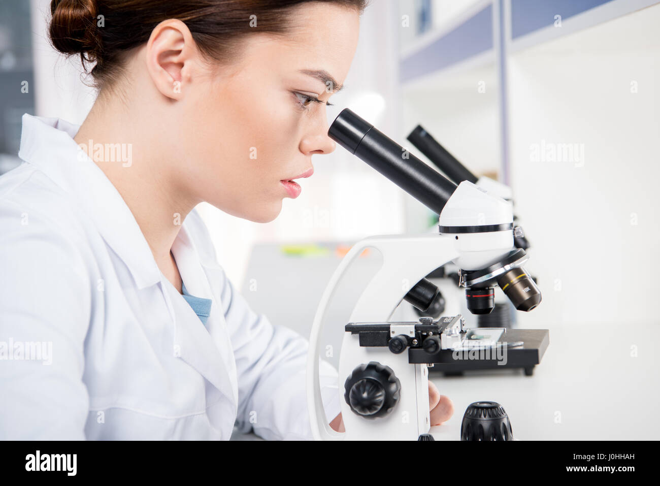 Profile of concentrated female scientist working with microscope in lab Stock Photo