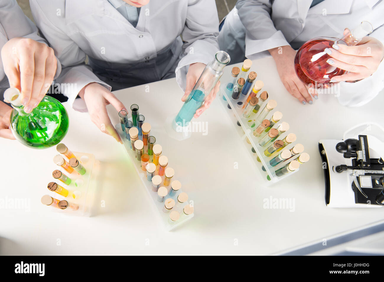 Top view of three female scientists holding chemical reagents in laboratory Stock Photo