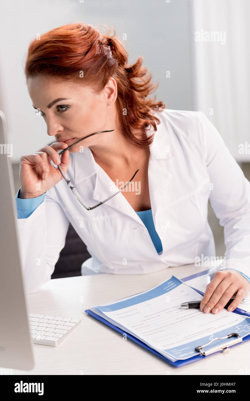 Concentrated female doctor holding eyeglasses while working with