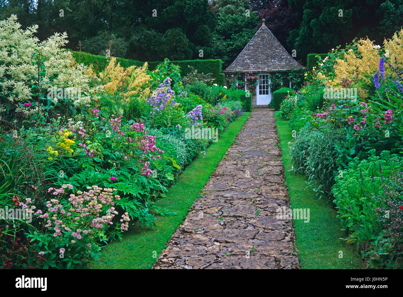 Path leading to garden room edged with colourful borders at Rodmarton Manor garden Stock Photo