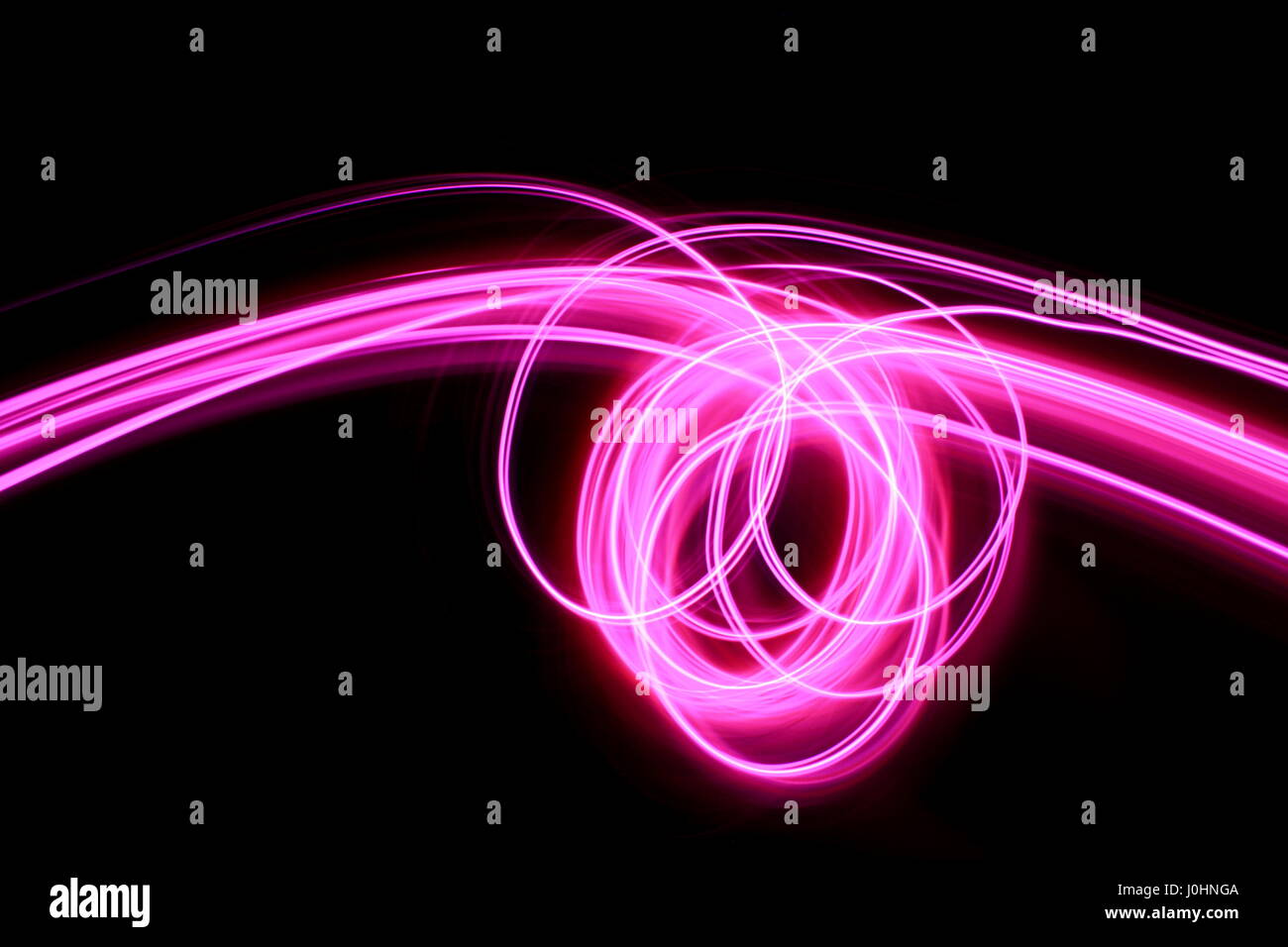 Pink light painting photography - long exposure photo of vibrant pink loops and swirls on black background.  Abstract light pattern. Stock Photo