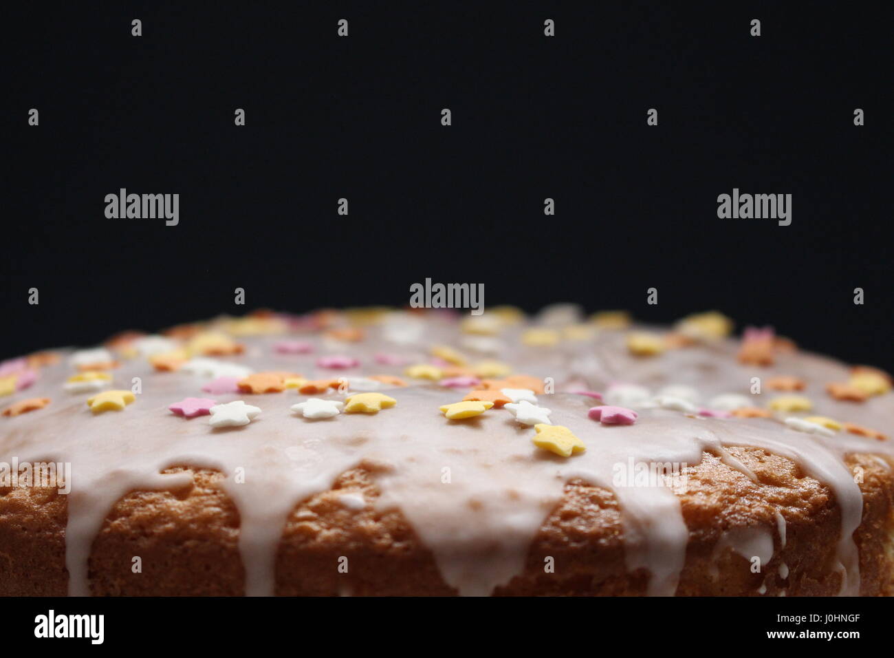 Birthday cake with runny icing, star decorations on a black background