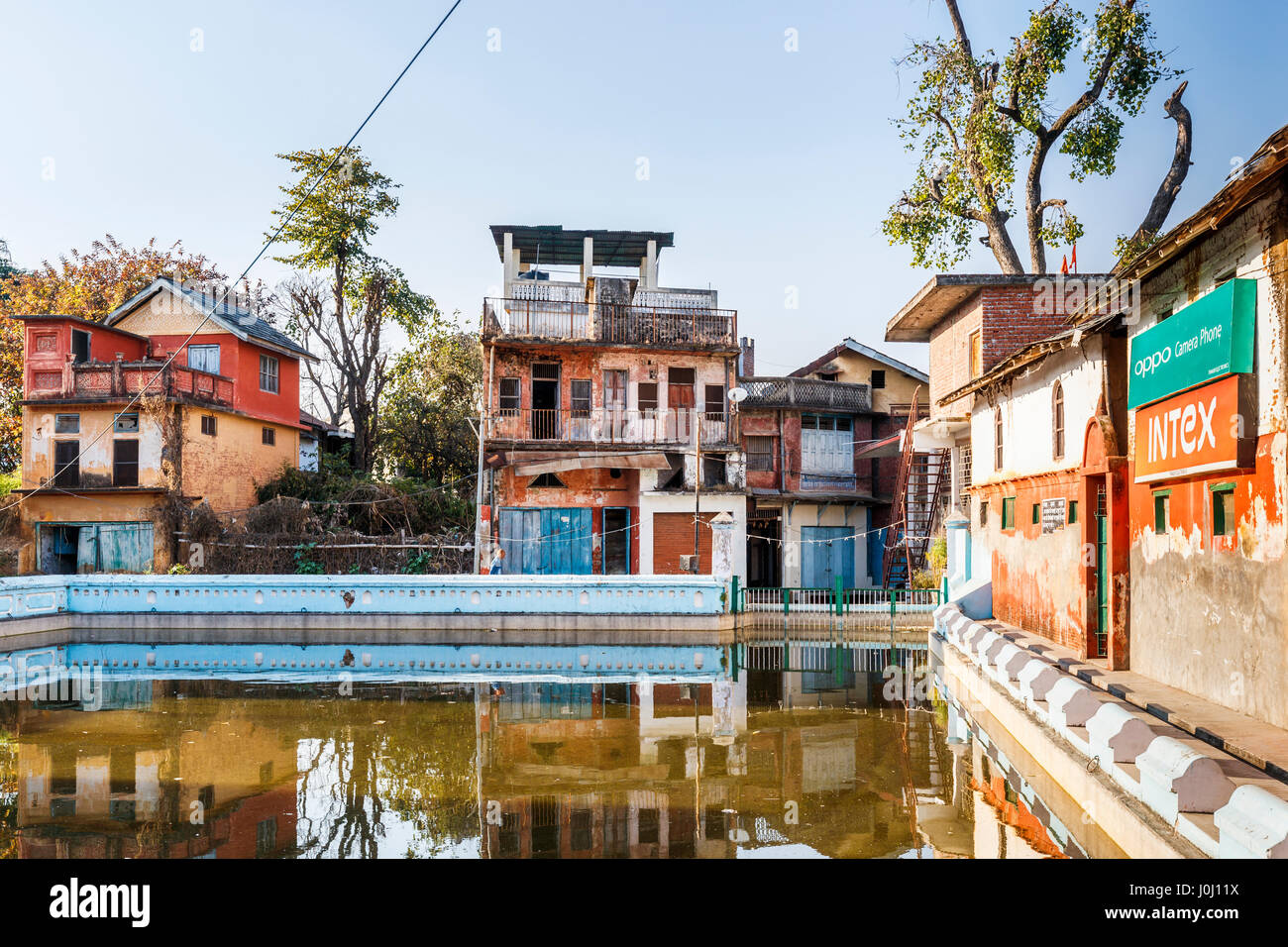 Dilapidated old buildings awaiting restoration reflected in the village tank (pond), Pragpur heritage village, Kagra district, Himachal Pradesh, India Stock Photo
