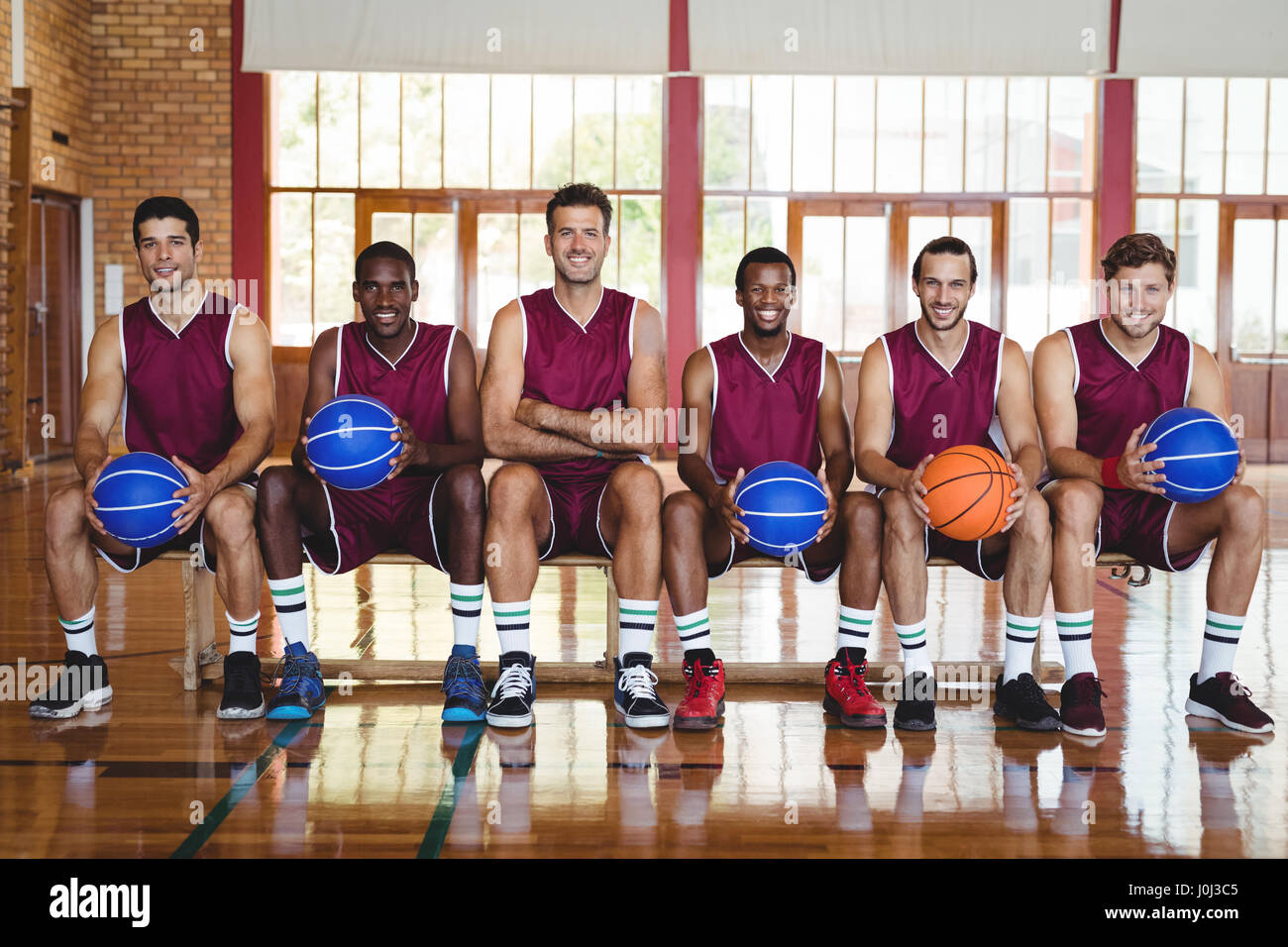 Portrait Of Smiling Basketball Players Sitting On Bench With Stock