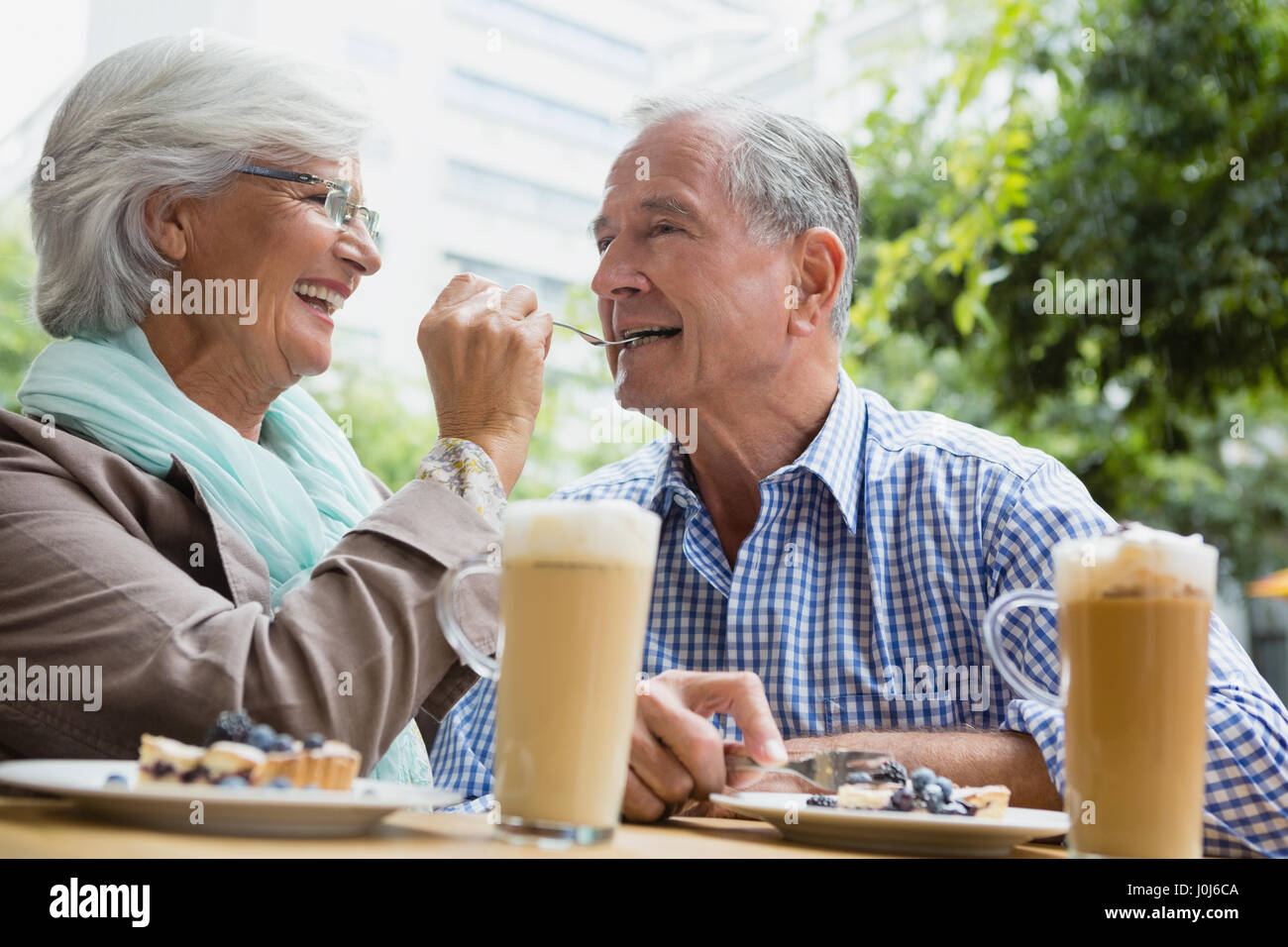Smiling senior woman feeding tart to man in outdoor cafÃƒÂ© Stock Photo