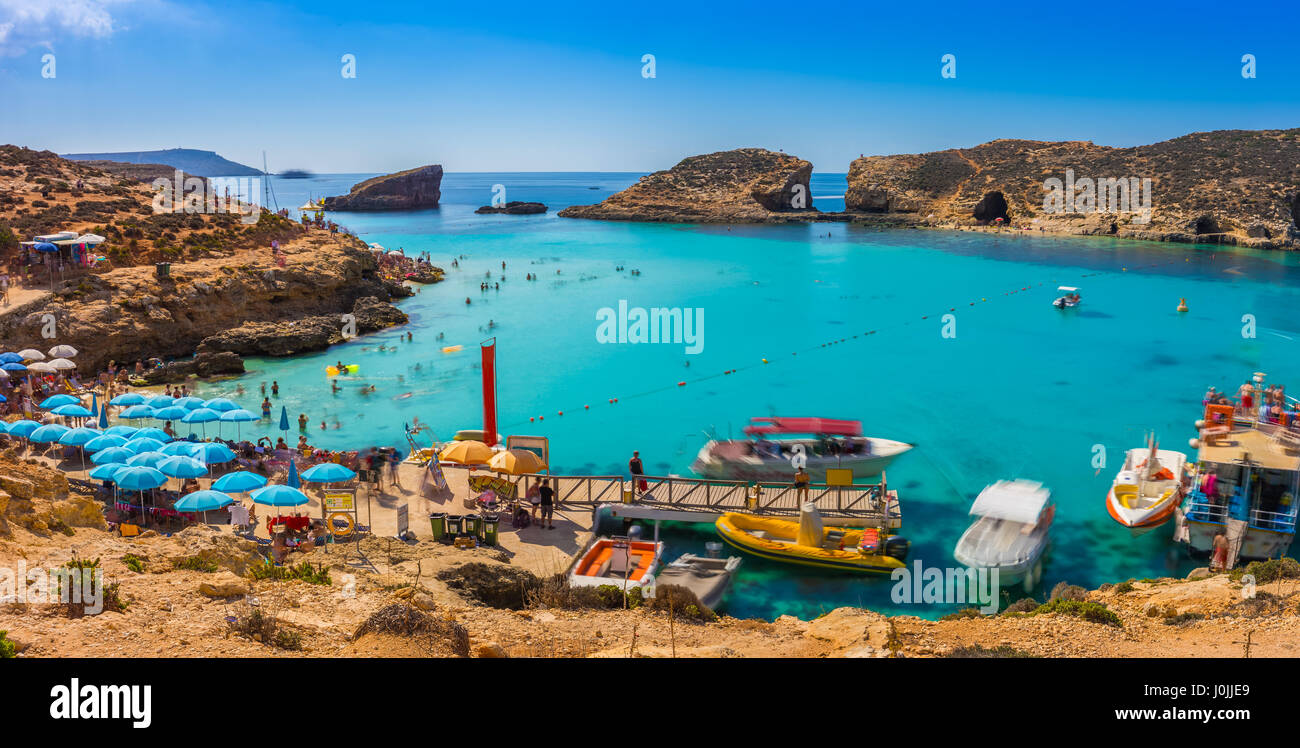 Comino, Malta - Tourists crowd at Blue Lagoon to enjoy the clear turquoise water on a sunny summer day with clear blue sky and boats on Comino island, Stock Photo