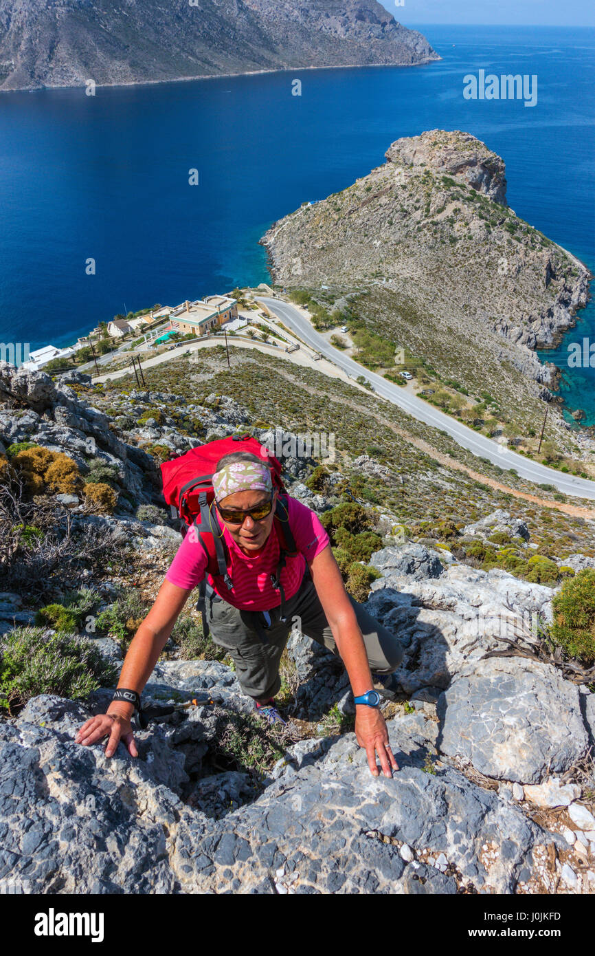 Female scrambling up rocks high above sea and road Stock Photo - Alamy