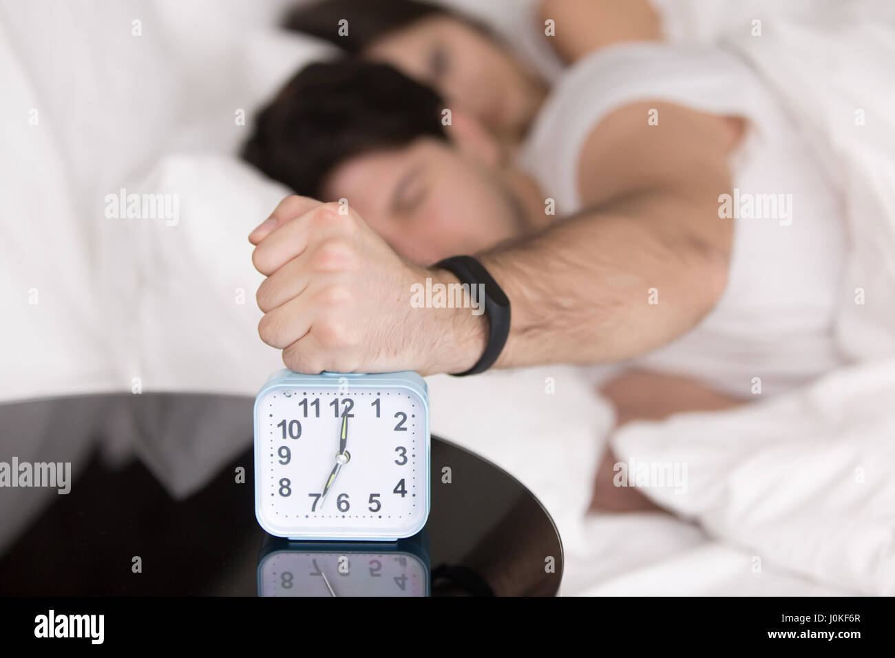 Couple waking up early, guy turning off annoying alarm clock Stock Photo