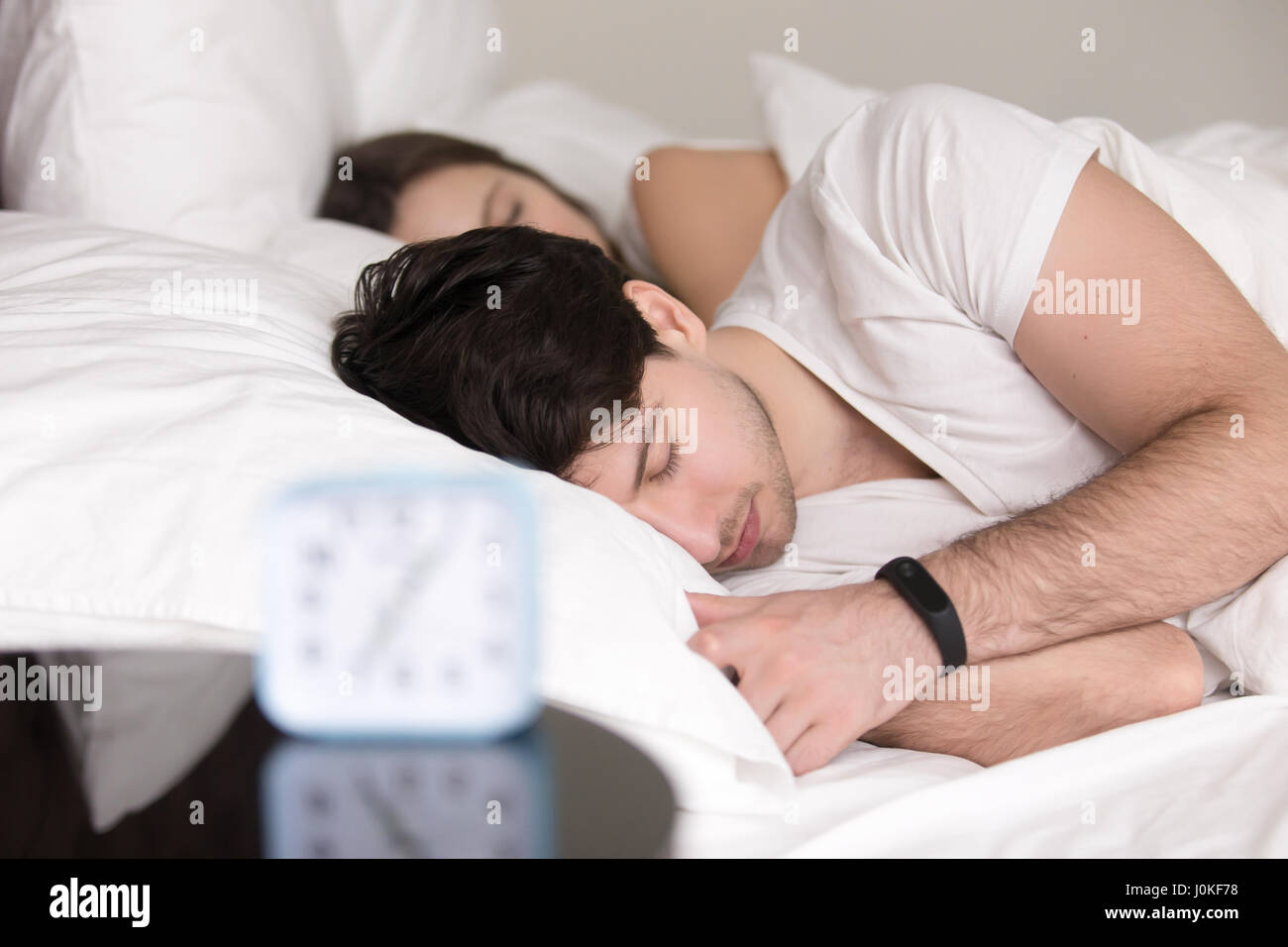 Couple lying asleep in bed, man wearing wristband smart watch Stock Photo