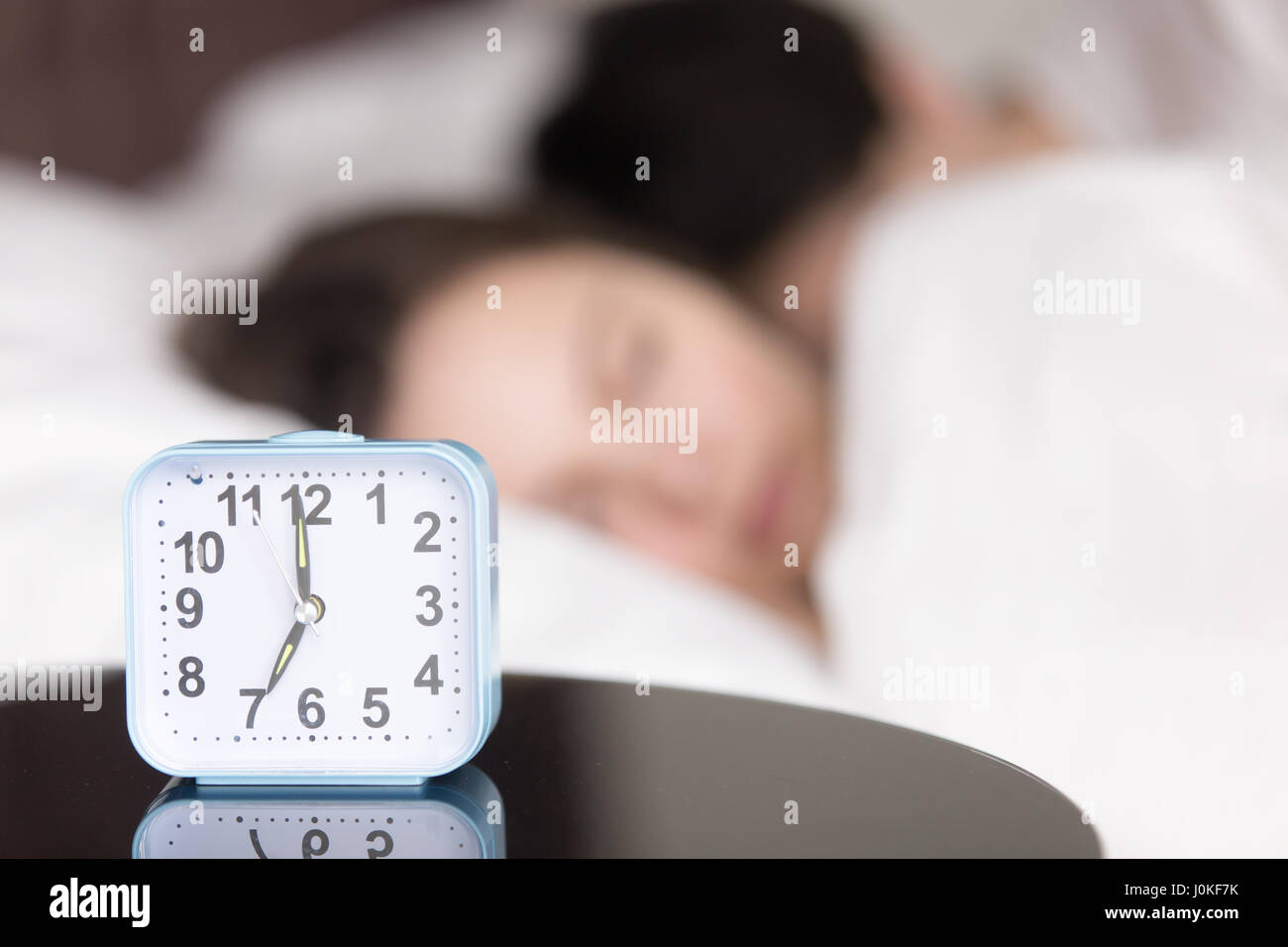 Alarm clock on table in front of sleeping young couple  Stock Photo