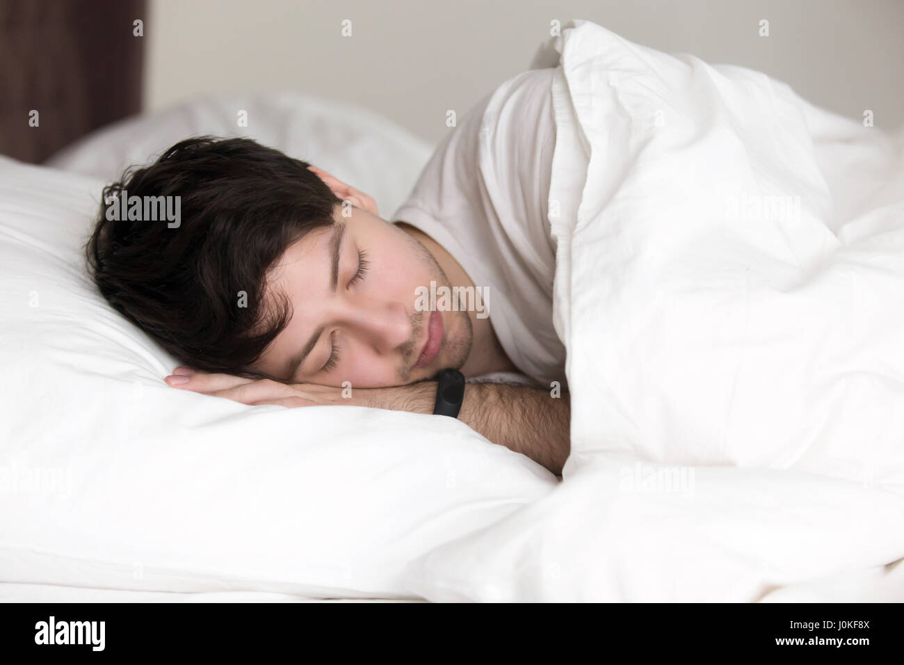 Handsome man asleep in bed wearing wristband for sleep tracking Stock Photo