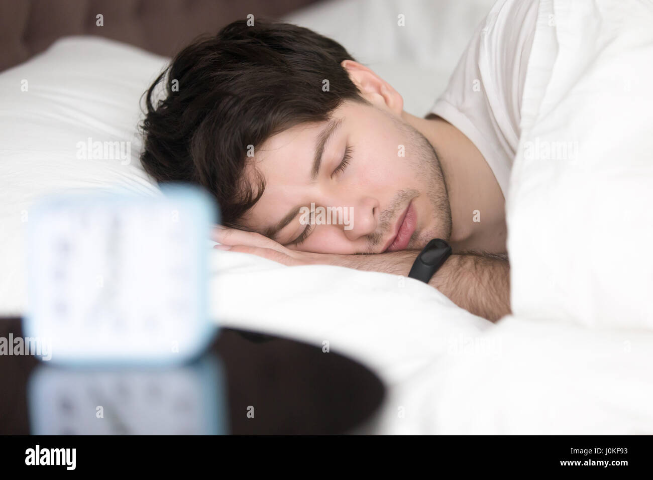 Young man sleeping next to alarm clock wearing smart wristband Stock Photo