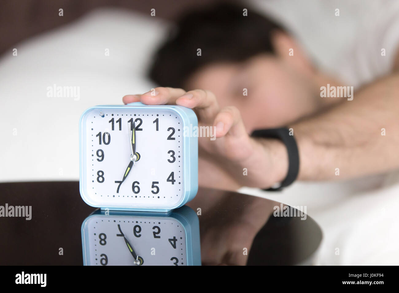 Awaking man in bed wearing wristband turning off alarm clock Stock Photo
