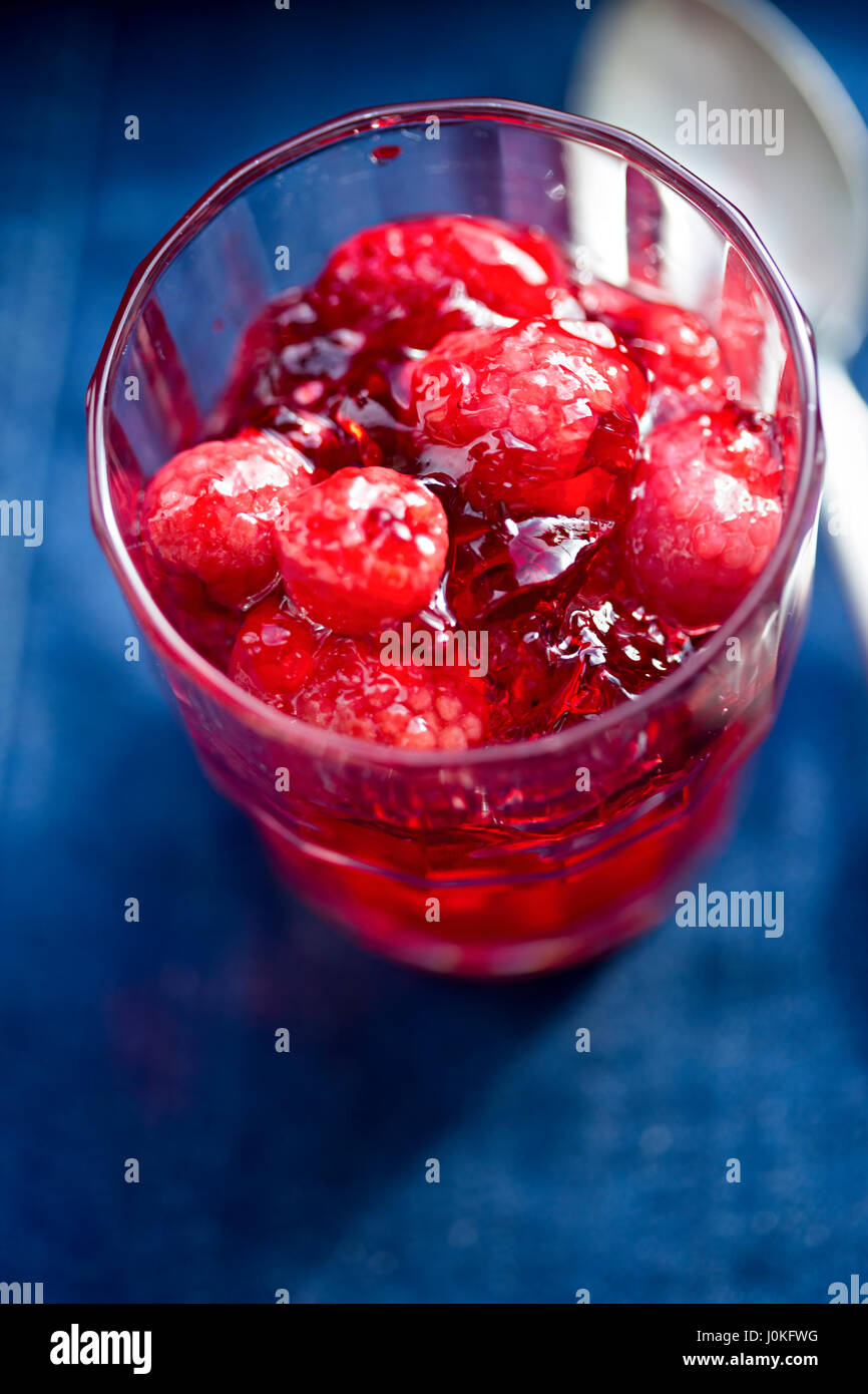 Raspberry jelly in glass on blue surface Stock Photo - Alamy