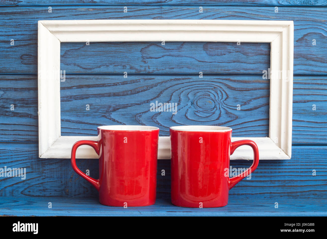 https://c8.alamy.com/comp/J0KGBB/white-frame-and-two-red-coffee-cups-on-a-background-of-blue-boards-J0KGBB.jpg