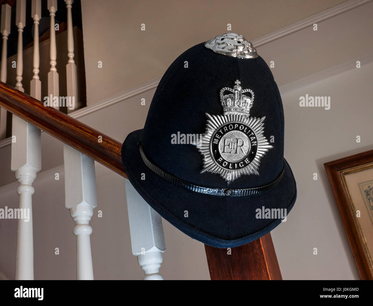 London Metropolitan Policeman's helmet and badge, on stair bannister in domestic 'end of day/interview' home living situation Stock Photo