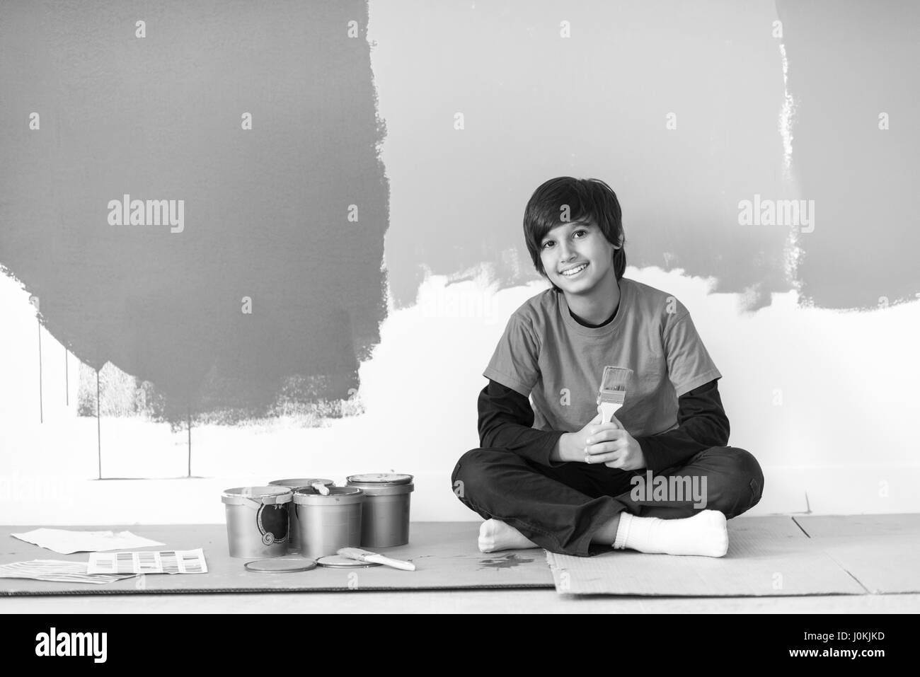 young boy painter resting after painting the wall, sitting on the floor