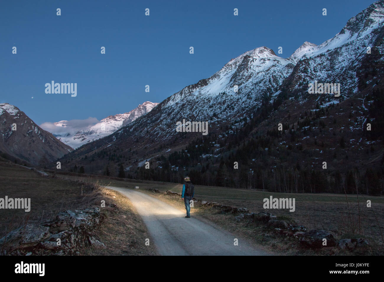 A man adventuring in the mountains at night exploring and looking at the stunning scenery wearing a headlight torch to see as walking at dawn Stock Photo