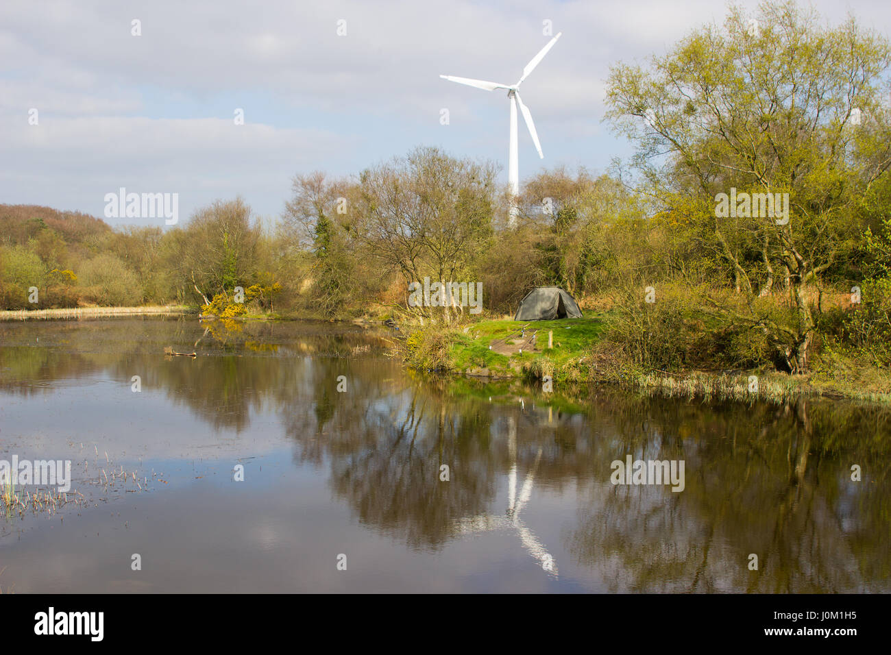 A two man tent pitched on a piece of ground beside the lake at the old lead mines workings in Conlig, County Down with a wind turbine in the backgroud Stock Photo