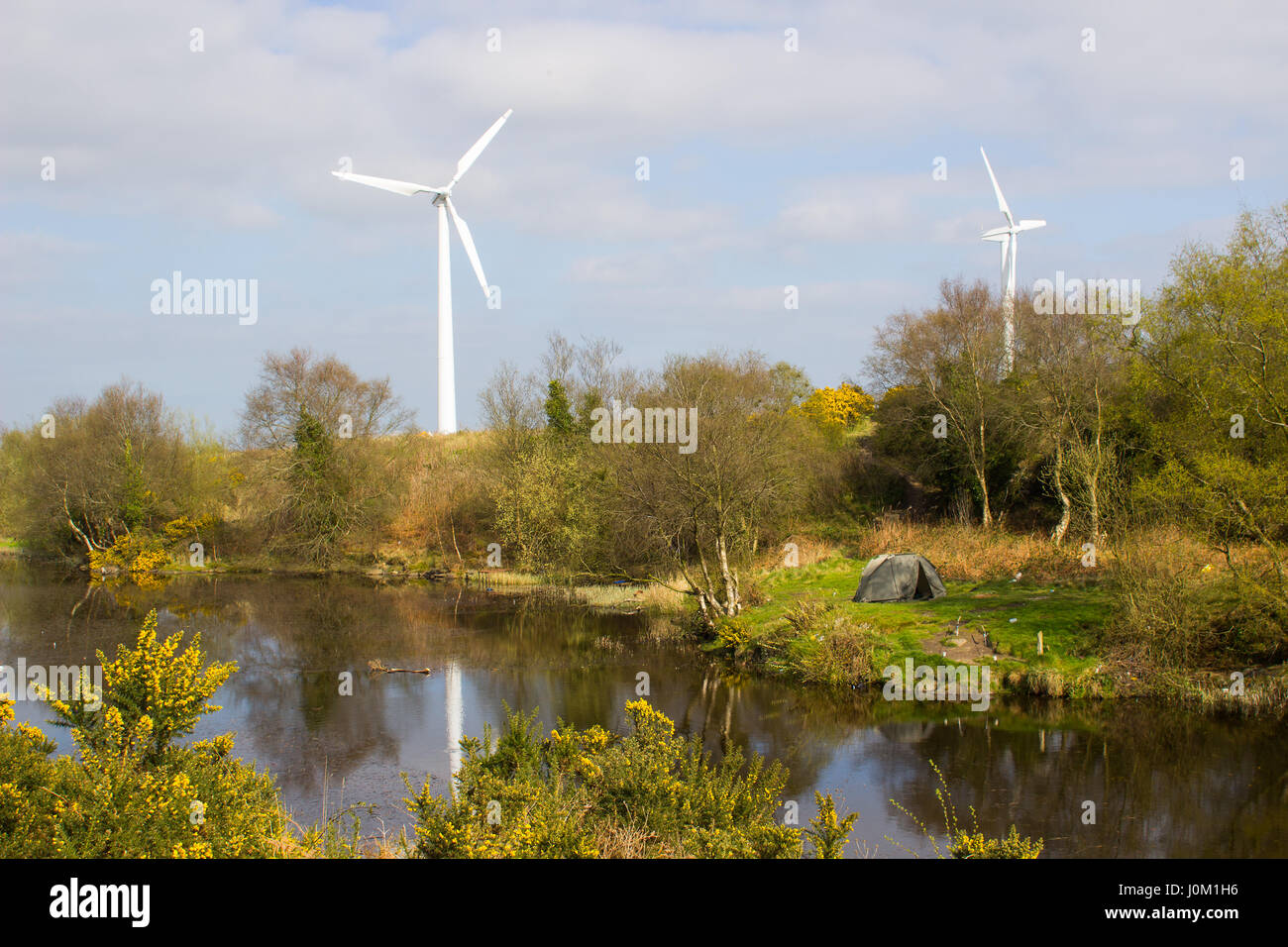 A two man tent pitched on a piece of ground beside the lake at the old lead mines workings in Conlig, County Down with a wind turbine in the backgroud Stock Photo