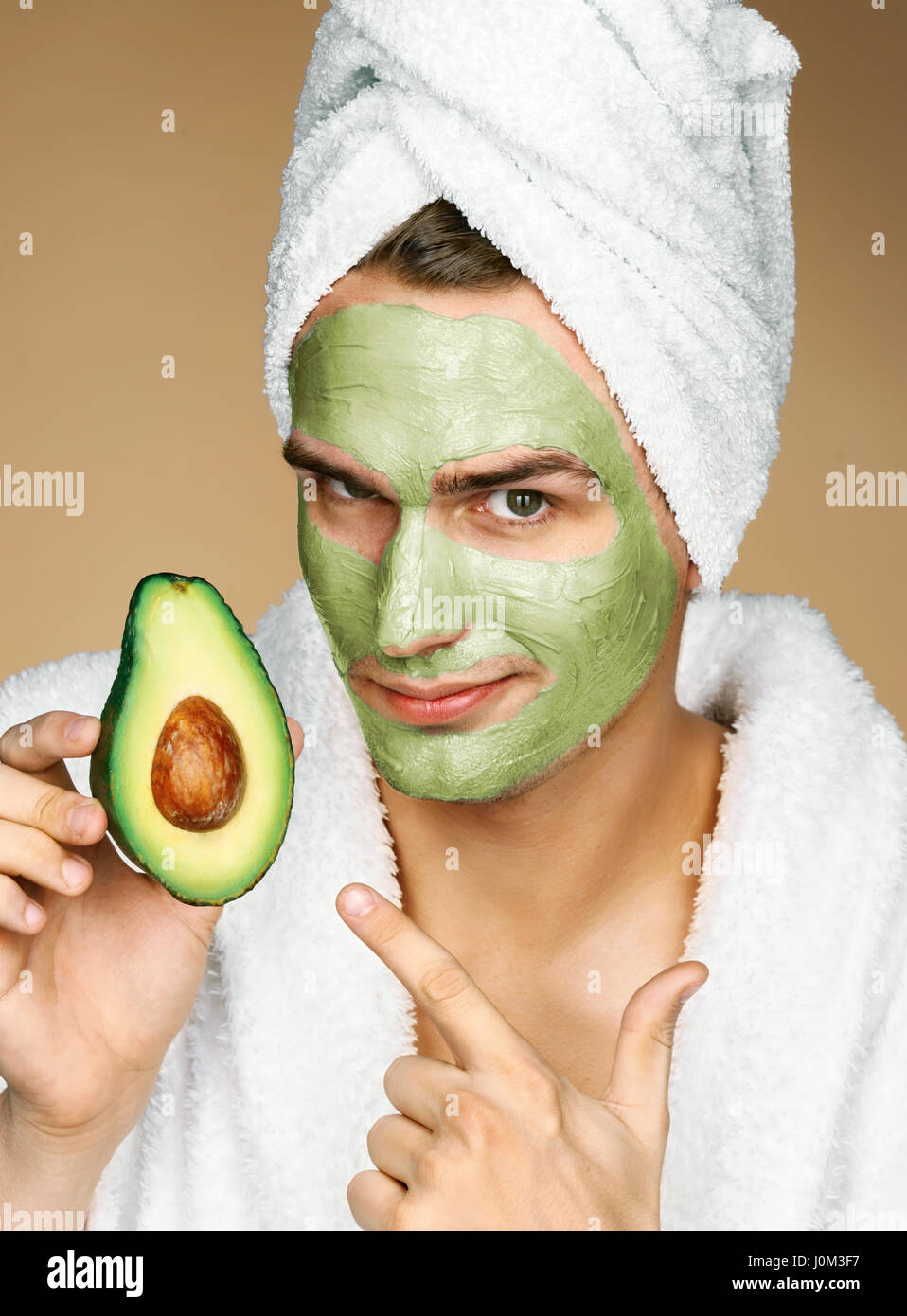 Man wearing towel and facial mask of avocado. Photo of well groomed man receiving spa treatments. Beauty & Skin care concept Stock Photo