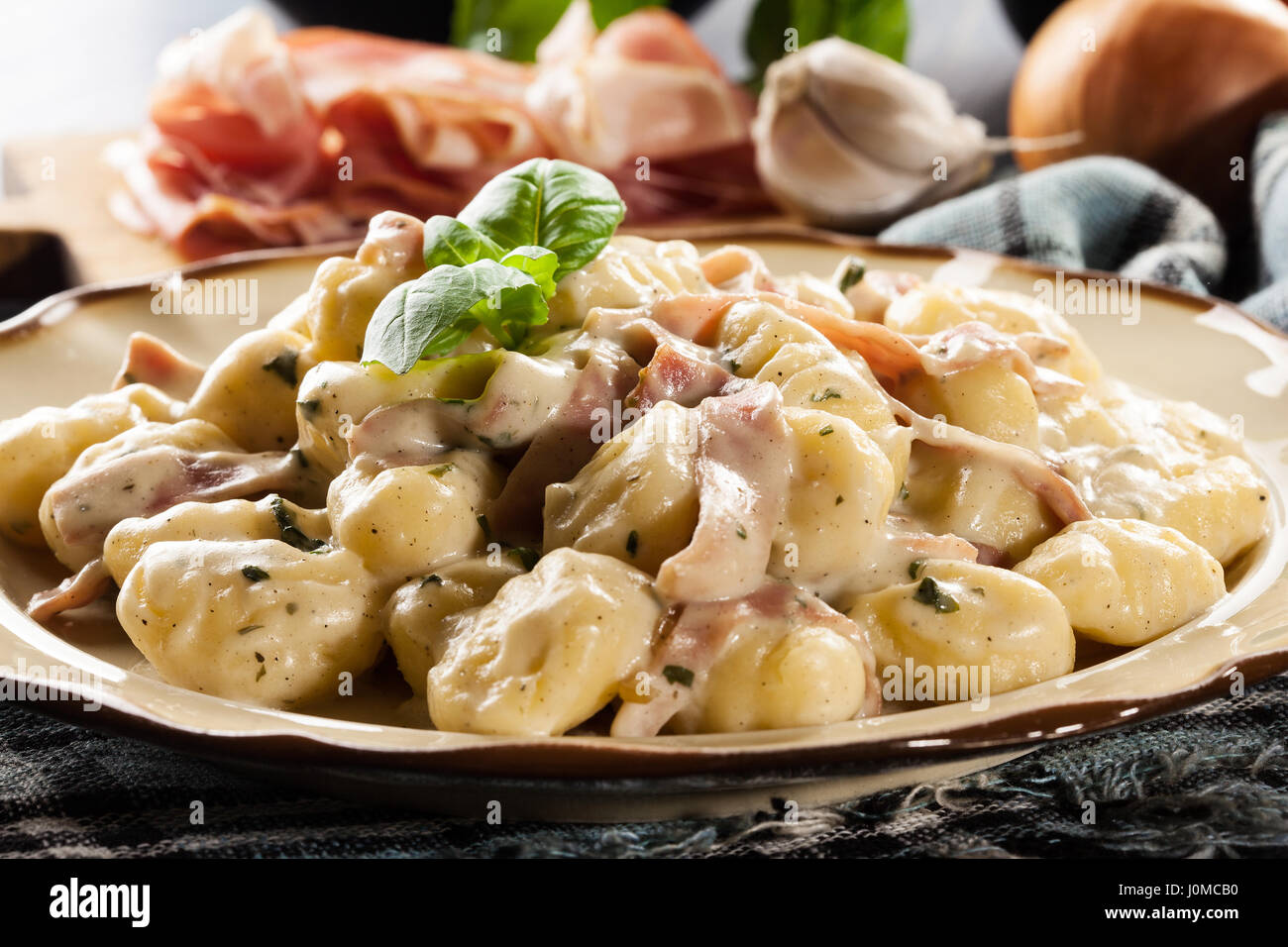 Potato gnocchi, Italian potato dumplings with cheese sauce, ham and basil on a plate Stock Photo