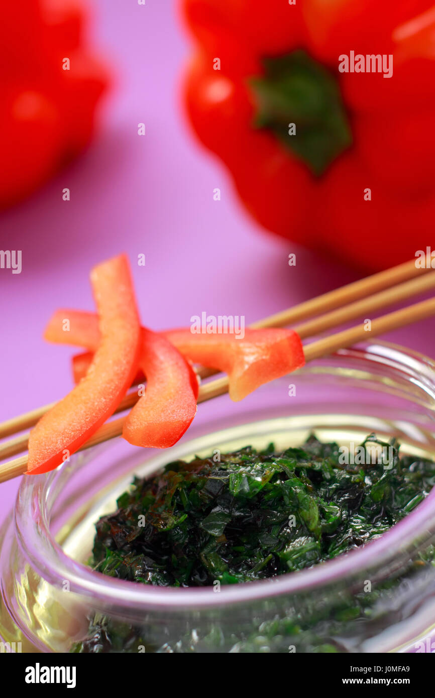 Herbal green dressing in glass bowl and red paprika parts with unfocused background Stock Photo