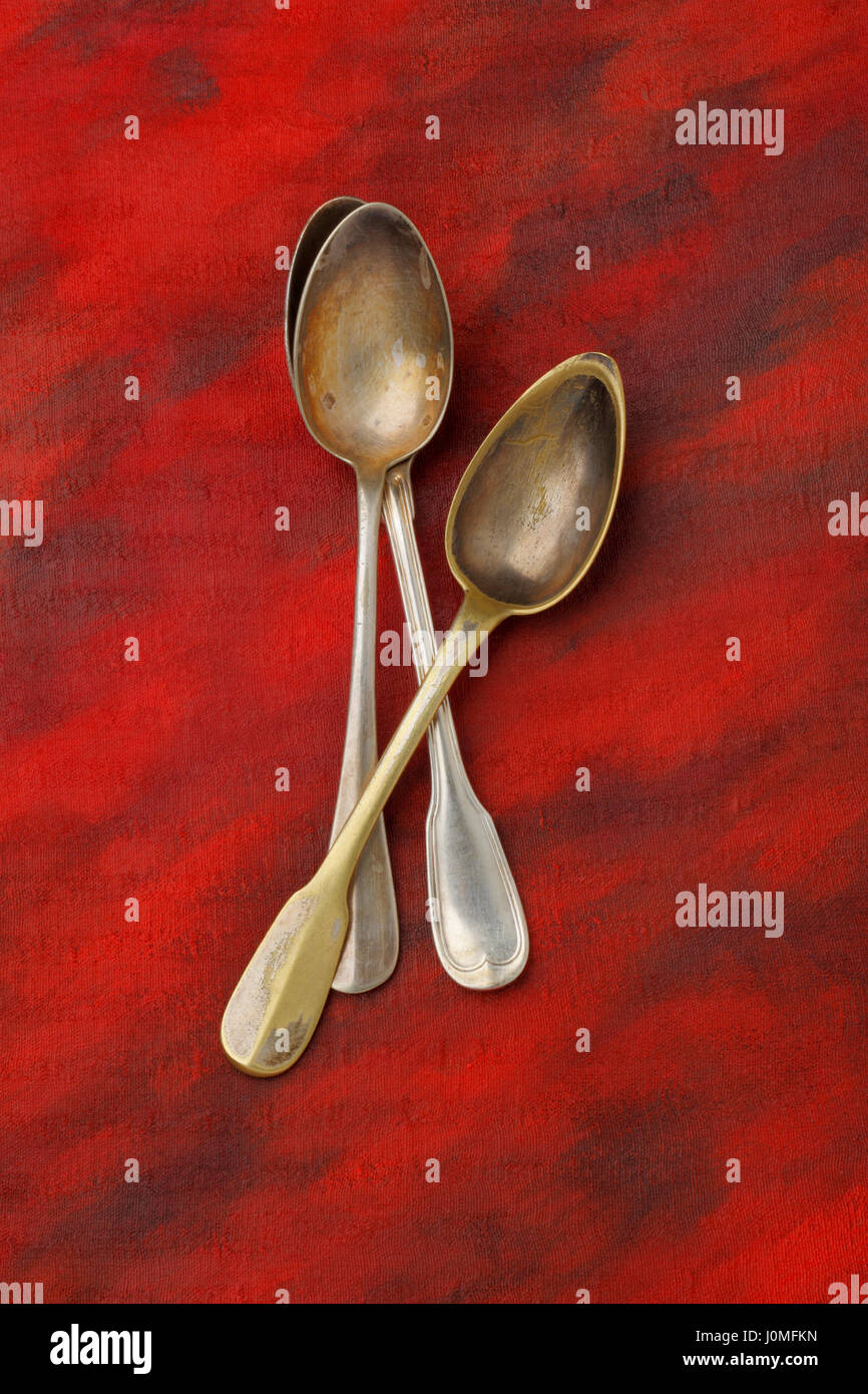 Pile of a three antique silver spoons over painted textile background. Overhead view. Stock Photo