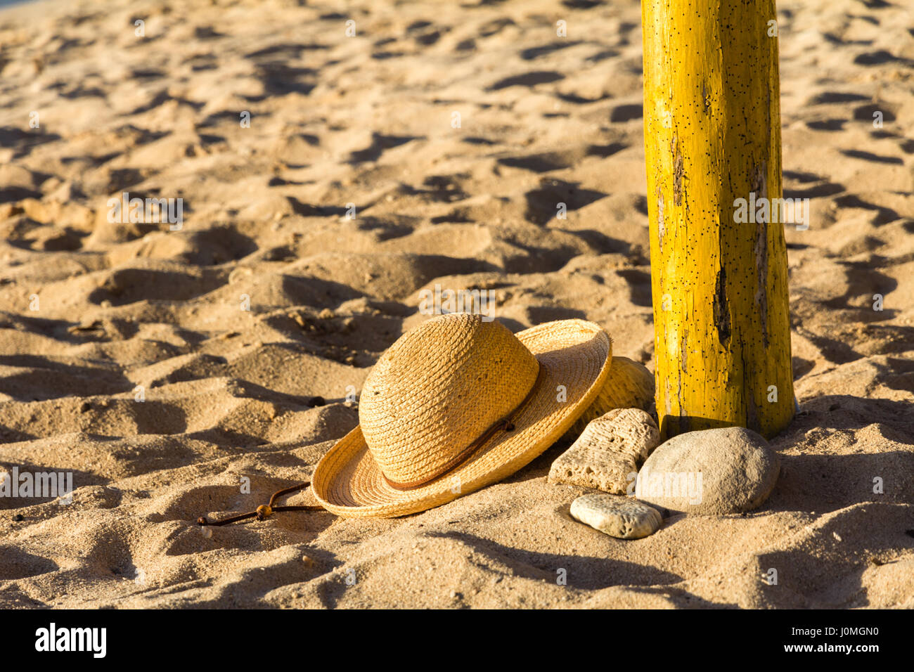Stylish straw hat at base of yellow wooden parasol pole on a sandy
