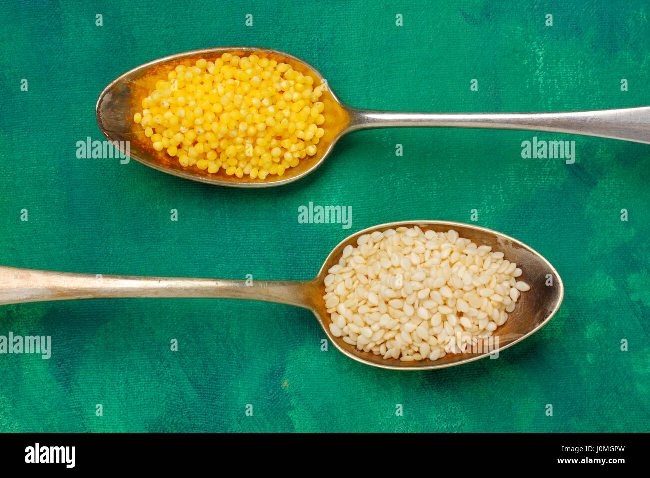 Two silver spoons filled with millet groats and sesame seeds. Close up, top view. Stock Photo