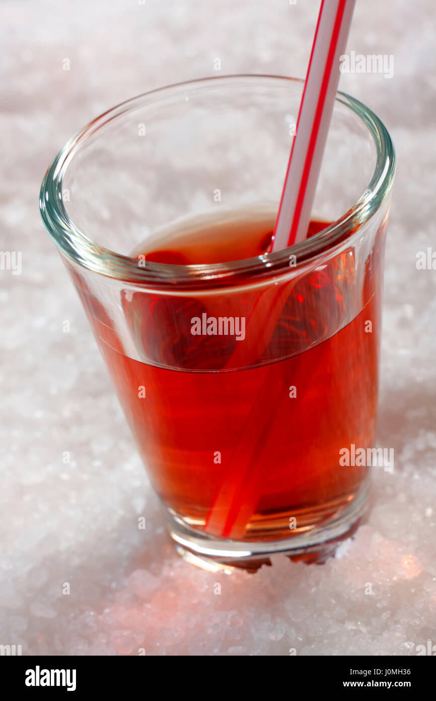 Red drink in glass on background from crumbled ice. Oblique frame. Stock Photo