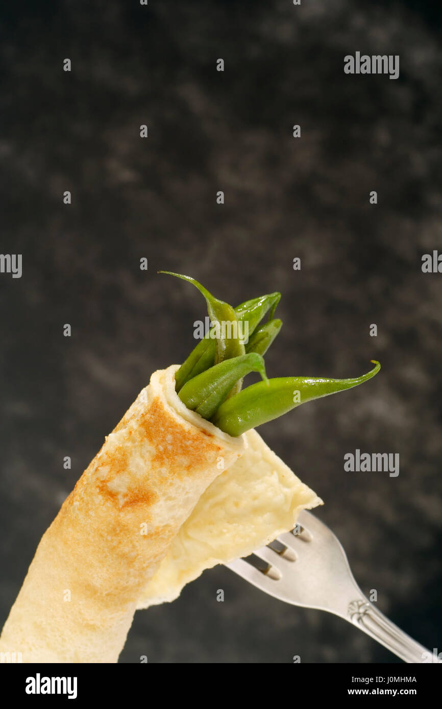 Cooked green bean's pods wrapped up in pancake on silver antique fork with copy space at top. Stock Photo