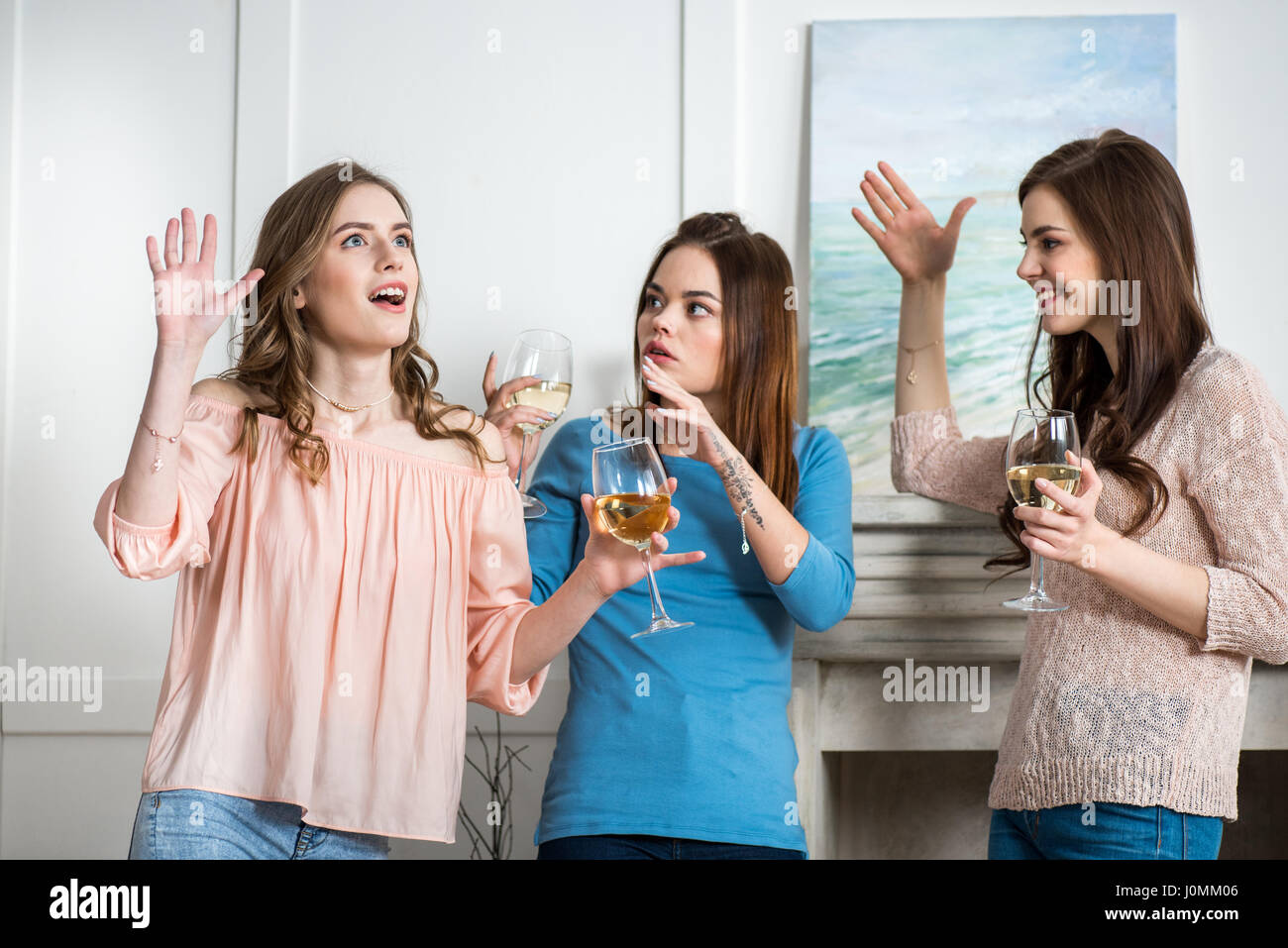 Three excited young attractive women holding glasses with white wine and gesticulating Stock Photo