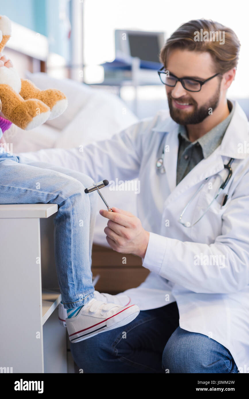 Smiling male doctor using reflex hammer on knee of little patient Stock