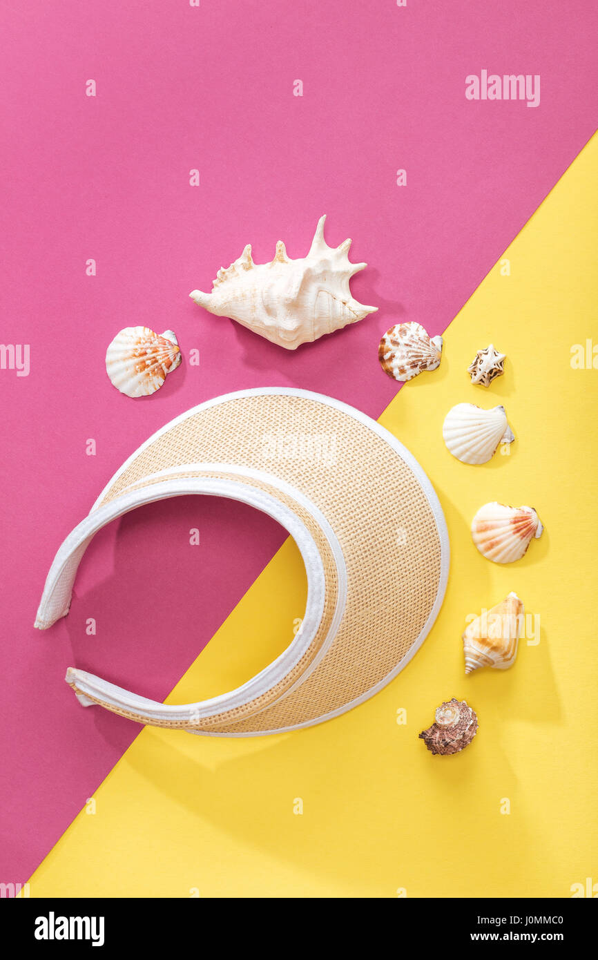 top view of baseball cap and shells on pink and yellow tabletop. Summer