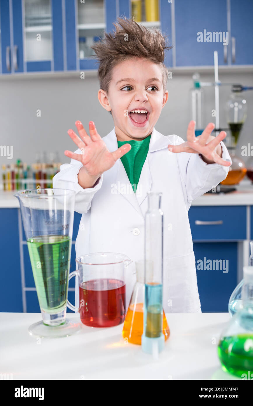 Excited little boy in lab coat making experiment in chemical laboratory