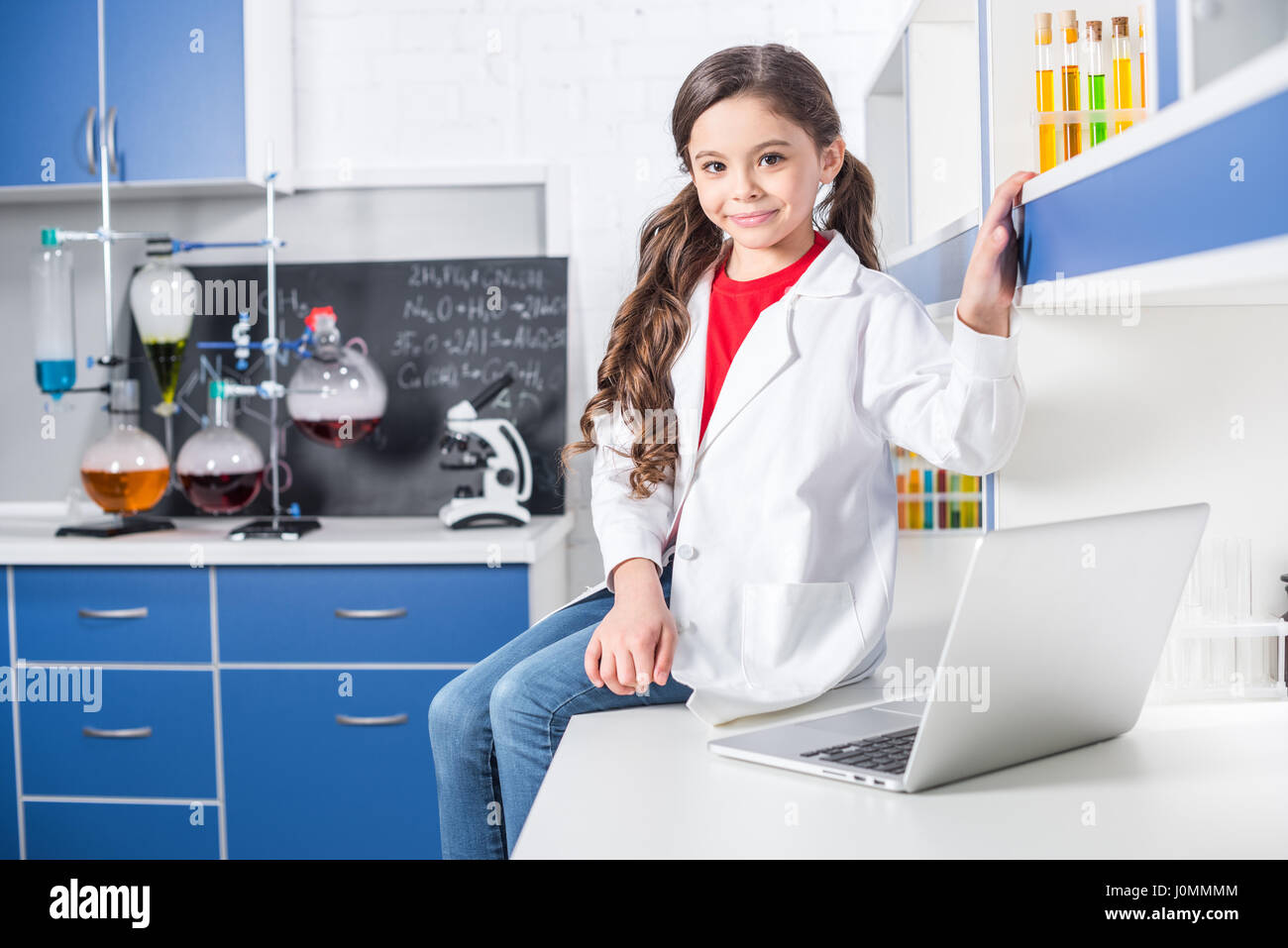 Beautiful little girl in lab coat using laptop in chemical laboratory