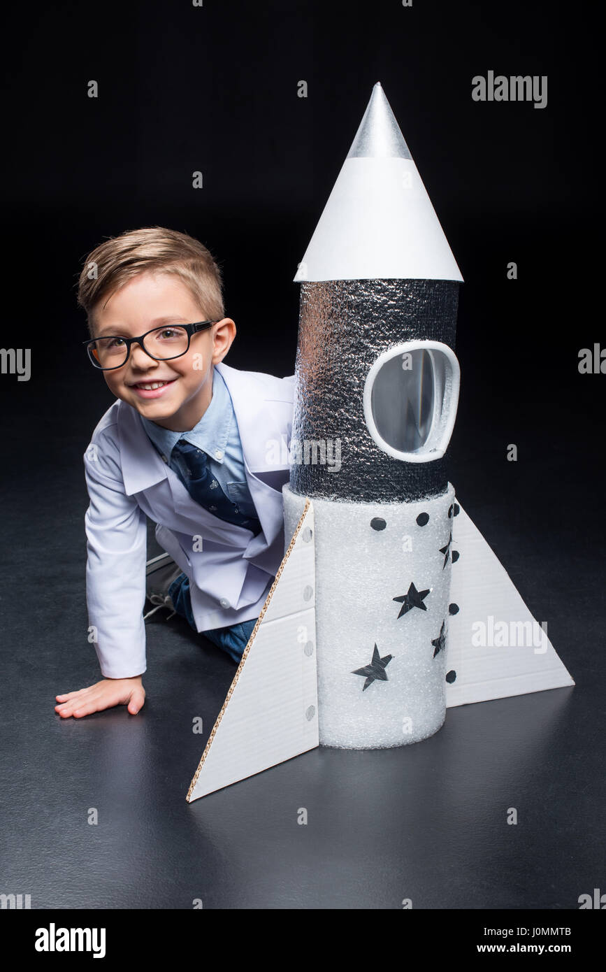 Little boy in white coat and eyeglasses playing with rocket and smiling at camera Stock Photo