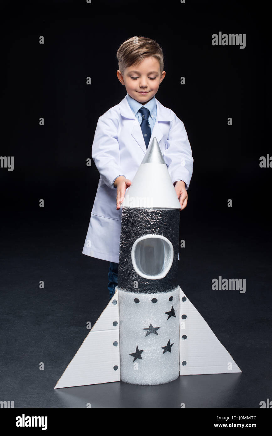 Smiling little boy in white coat playing with rocket on black Stock Photo