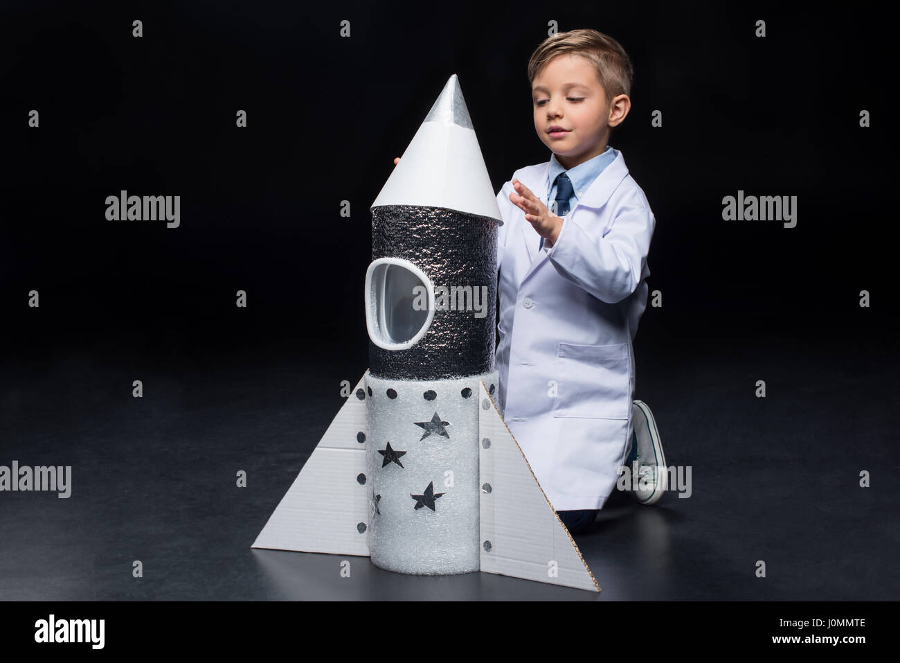 Cute little boy in white coat kneeling and playing with toy rocket Stock Photo