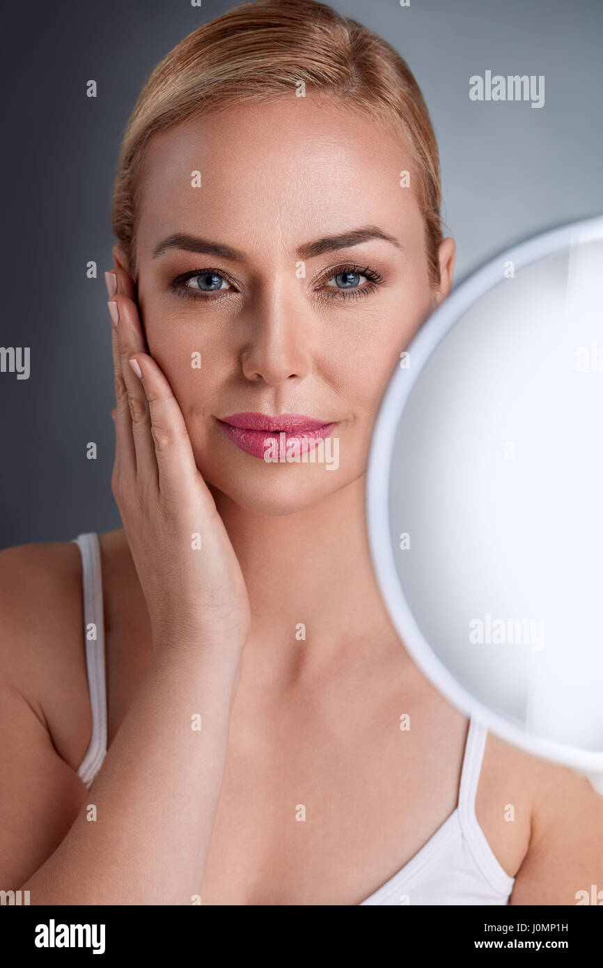 Beautiful woman with mirror looking her perfect skin Stock Photo