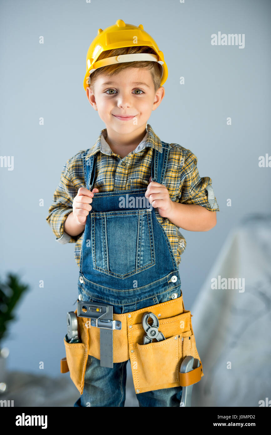 Cute little boy in hard hat and tool belt smiling at camera Stock Photo