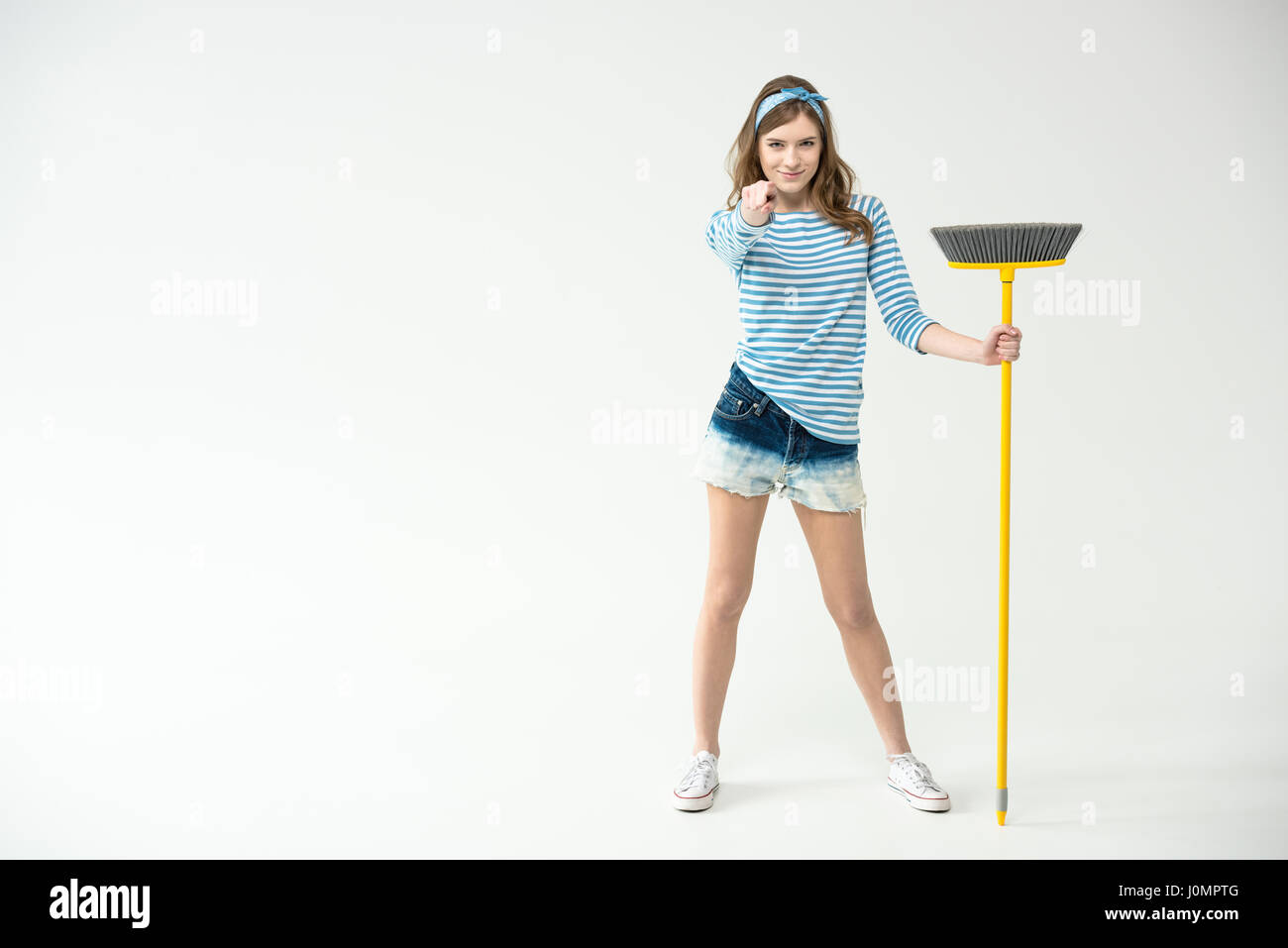 Attractive young woman holding broom and pointing at camera Stock Photo