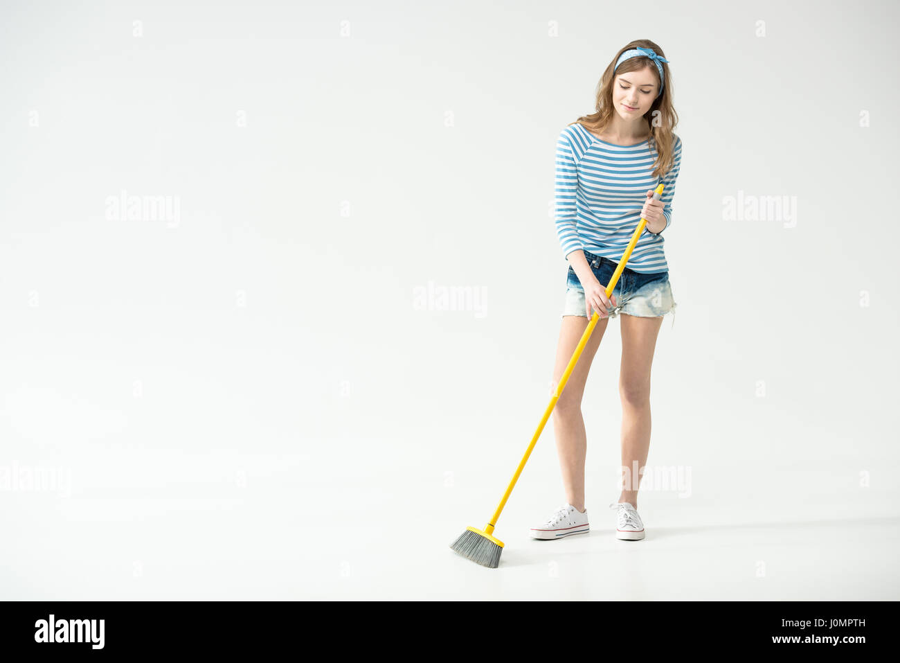 Beautiful young woman sweeping with broom on grey Stock Photo