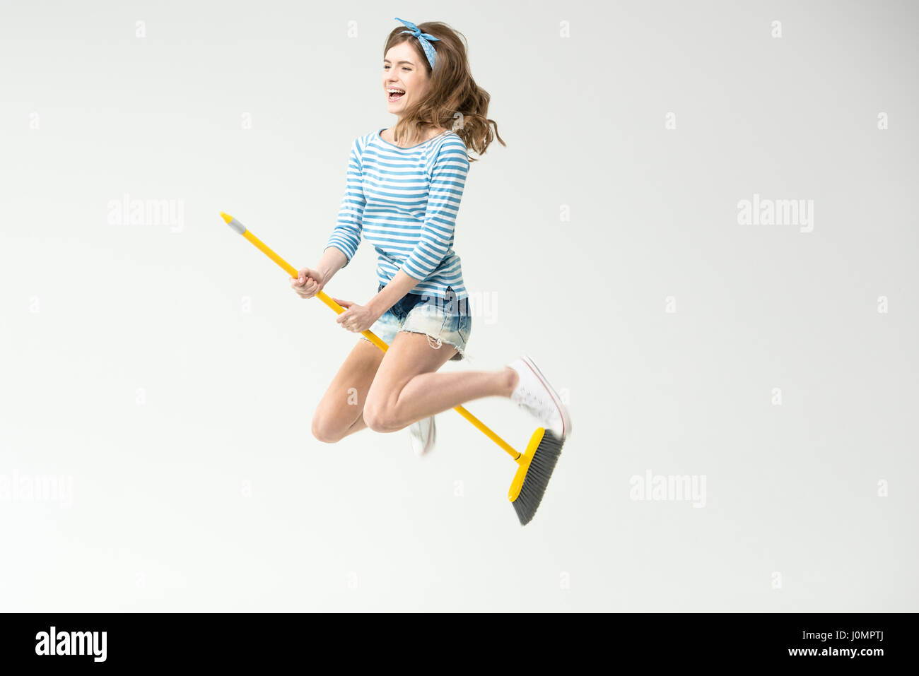 Happy beautiful young woman flying on broom on grey Stock Photo - Alamy