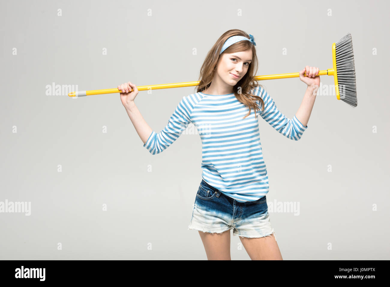 Beautiful young woman holding broom on shoulders and smiling at camera
