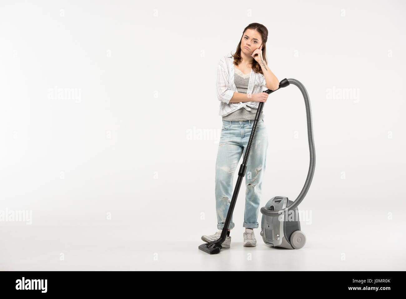 Thoughtful young woman standing with vacuum cleaner on grey Stock Photo