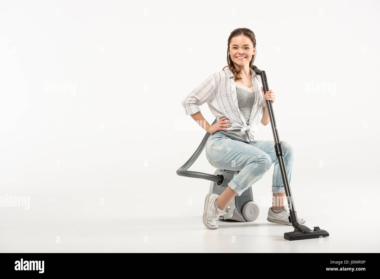 Attractive young woman sitting on vacuum cleaner and smiling at camera Stock Photo
